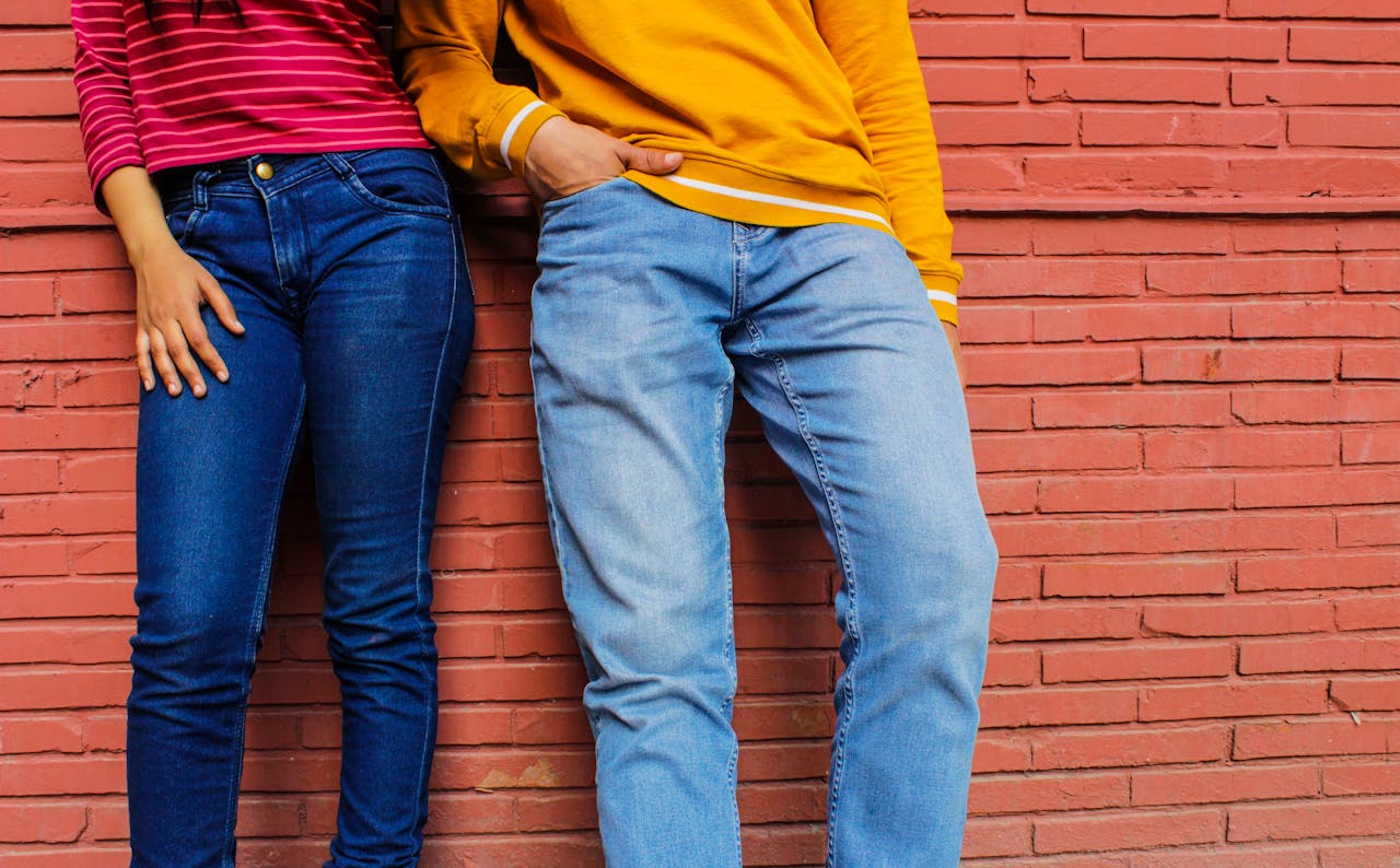 Two people in casual attire and denim jeans against a brick wall.